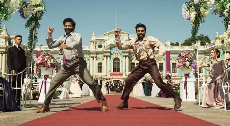 Bheem and Ram dance on the red carpet in front of the palace.