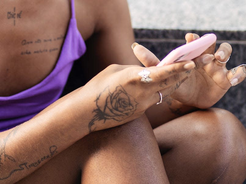 black trans woman with several tattoos looking at her phone and smiling