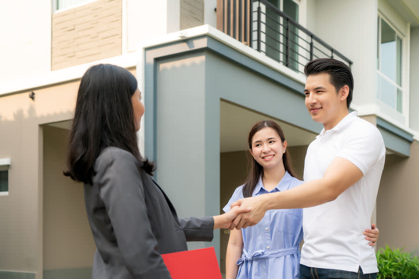 Happy Asian couple looking for their new house and shake hands with real estate broker after a deal. Young couple handshaking real estate agent after signing contract for buy house.