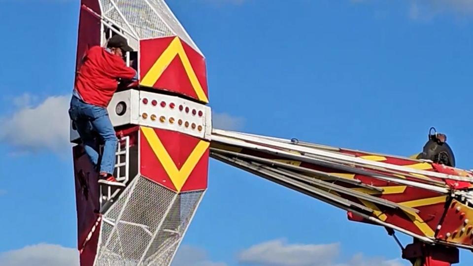 A ride operator hangs from an amusement park ride at the 54th annual Groves Pecan Festival in Groves, Texas after a gust of wind launched the ride's car into the air on Oct. 15, 2023.