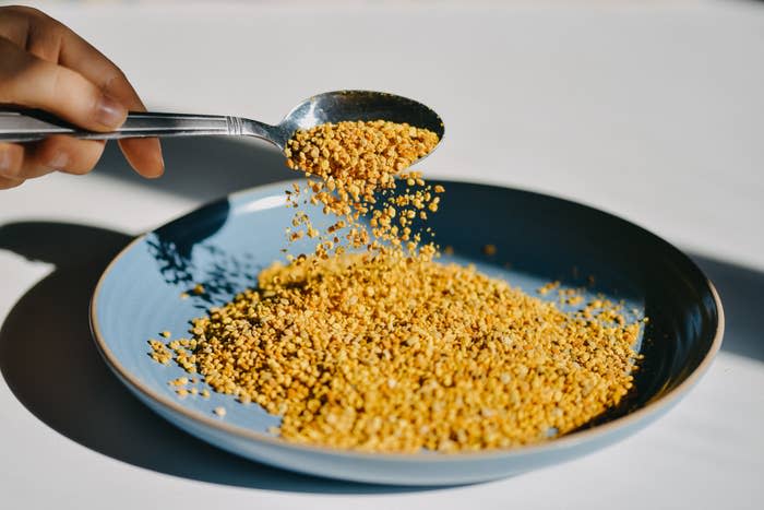 a hand holding a spoon of bee pollen over a bowl