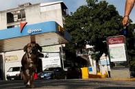 A dog walks with its owner in front of a gas station belonging to Venezuela's state oil company PDVSA in Caracas, Venezuela July 21, 2016. Picture taken July 21, 2016. REUTERS/Carlos Jasso