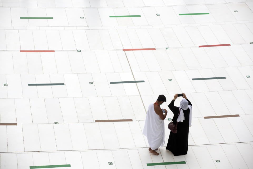 A Muslim pilgrim couple takes mobile shots at the Grand Mosque, as they stand on social distancing signs, a day before the annual hajj pilgrimage, Saturday, July 17, 2021. The pilgrimage to Mecca required once in a lifetime of every Muslim who can afford it and is physically able to make it, used to draw more than 2 million people. But for a second straight year it has been curtailed due to the coronavirus with only vaccinated people in Saudi Arabia able to participate. (AP Photo/Amr Nabil)