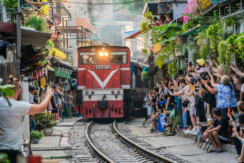 View of train passing through a narrow street of the Hanoi Old Quarter with tourists flanking the train tracks