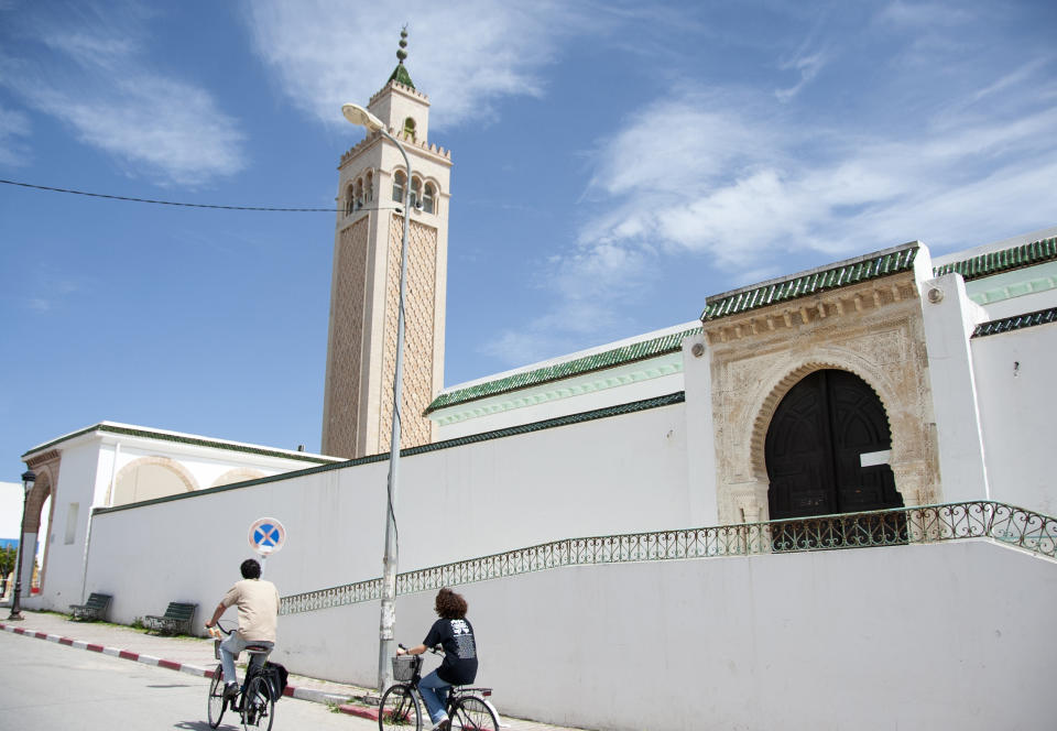 People ride their bicycle past a closed mosque in La Marsa district, just outside Tunis, Monday, May, 10, 2021. Tunisia announced on Friday strict new measures to try to contain the spread of the coronavirus, with the prime minister saying that the health system risks collapsing if something is not done. Houses of prayer are being ordered closed starting Sunday for a week, along with outdoor markets and large stores and malls. Shops selling food can remain open. (AP Photo/Hassene Dridi)