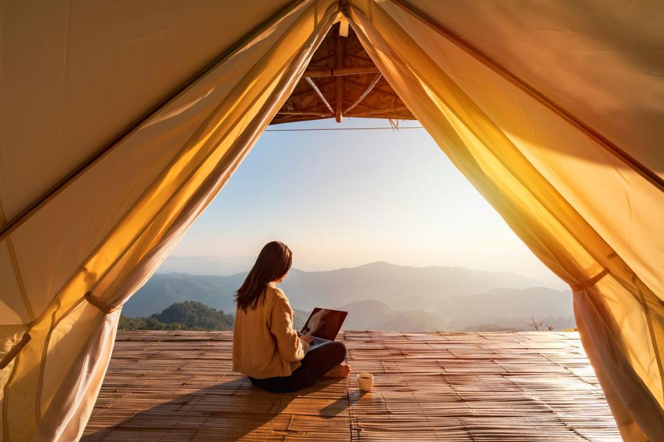 young woman freelancer traveler working online using laptop and enjoying the beautiful nature landscape with mountain view at sunrise