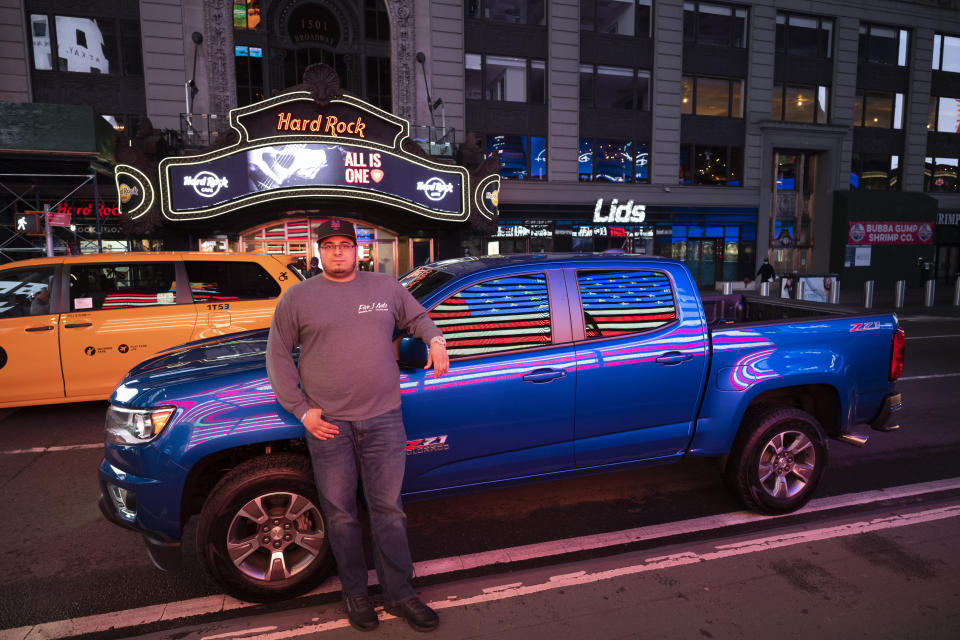 In this April 29, 2020 photo, Steve Cruz poses with his Chevy Colorado in New York's Times Square during the coronavirus pandemic. Car mavens normally wouldn't dare rev their engines in Midtown, but now they're eagerly driving into the city to take photos and show off for sparse crowds walking through the commercial hub. (AP Photo/Mark Lennihan)