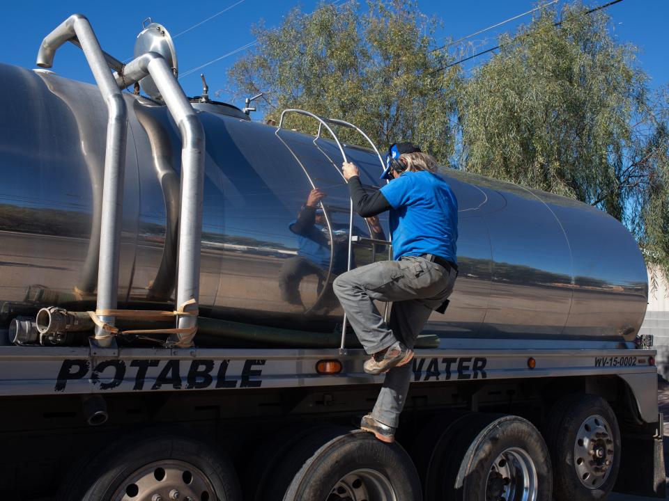 Man climbing down the side of a water-hauling truck.