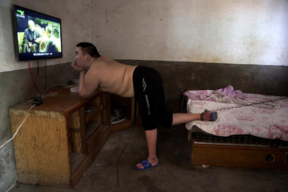 In this July 12, 2018, photo, Li Mingming, whose foot is chained to a bed, a practice sometimes employed by families in rural China to keep mentally disabled relatives from wandering away, watches television in this home in Gucheng village in central China's Henan province. The AP spoke to the family Marip Lu, a young woman from Myanmar, accused of abusing her. The father, Li Qinggong, and the mother, Xu Ying, both denied Marip Lu had been abused or raped, and insisted she had not been purchased. But neither was able to explain how she'd ended up in their faraway village, or how she allegedly met and "married" their mentally disabled son, Li Mingming, seen in this photo. (AP Photo/Ng Han Guan)