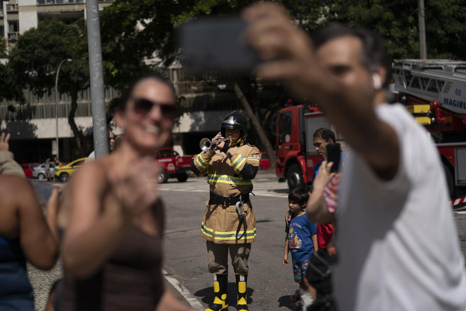 Residents take a selfie with the firefighter Elielson Silva playing his trumpet, after he performed from the top of a very tall ladder for residents cooped up at home during a lockdown to help contain the spread of the new coronavirus in Rio de Janeiro, Brazil, April 5, 2020. (AP Photo/Leo Correa)