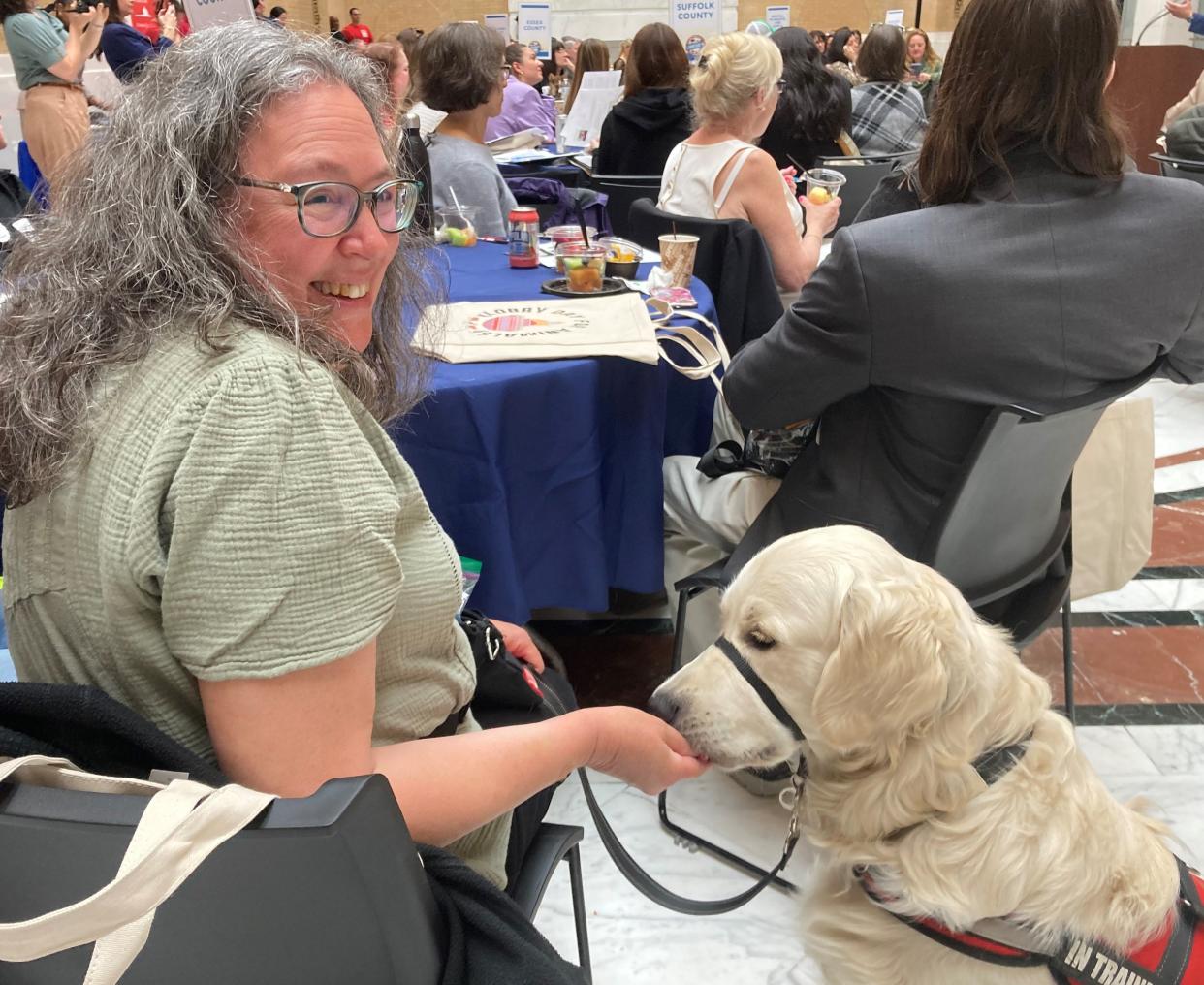 Odin, of Needham, is offered a treat by Betty Waterman, who is training the golden retriever to be a service dog for a person with disabilities. The two, along with husband Ernie Waterman, attended Animal Advocacy Day Tuesday at the State House.