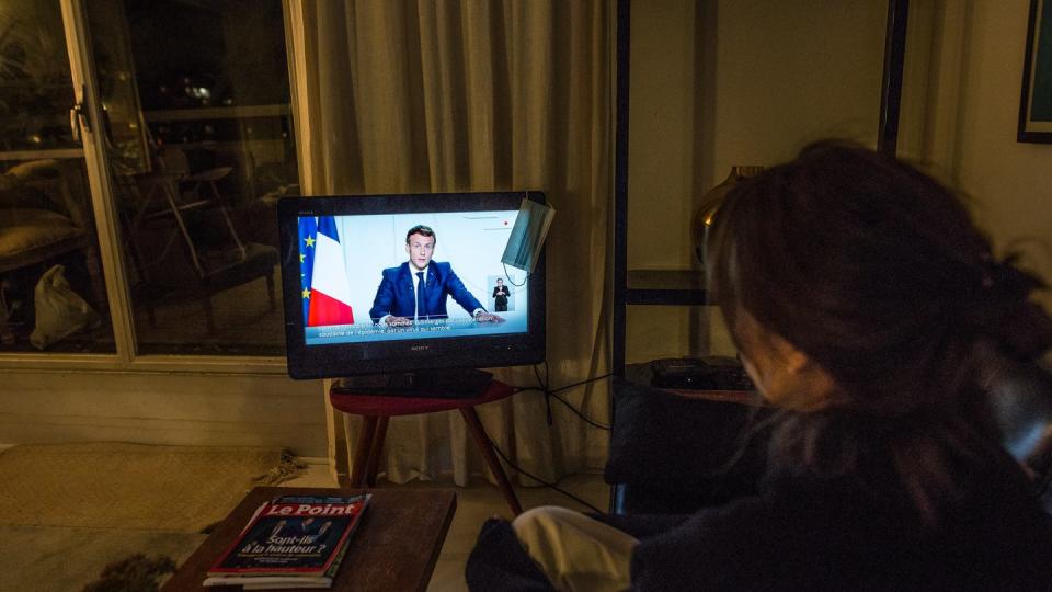 Eine Frau verfolgt in Paris die TV-Ansprache von Staatspräsident Emmanuel Macron.