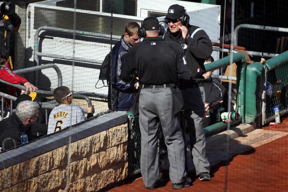 First base umpire Bob Davidson, right, and home plate umpire John Hirschbeck, center, talk over headsets as a pickoff safe call at first base is reviewed in the tenth inning of an opening day baseball game against the Chicago Cubs on Monday, March 31, 2014, in Pittsburgh. The safe call was overturned and Cubs' Emilio Bonifacio was ruled out. The Pirates won 1-0 in ten innings. (AP Photo/Gene J. Puskar)