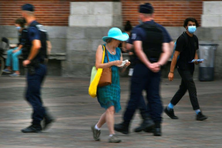 Une femme tient un masque alors qu'elle passe près de policiers à Toulouse, le 21 août 2020 - GEORGES GOBET © 2019 AFP