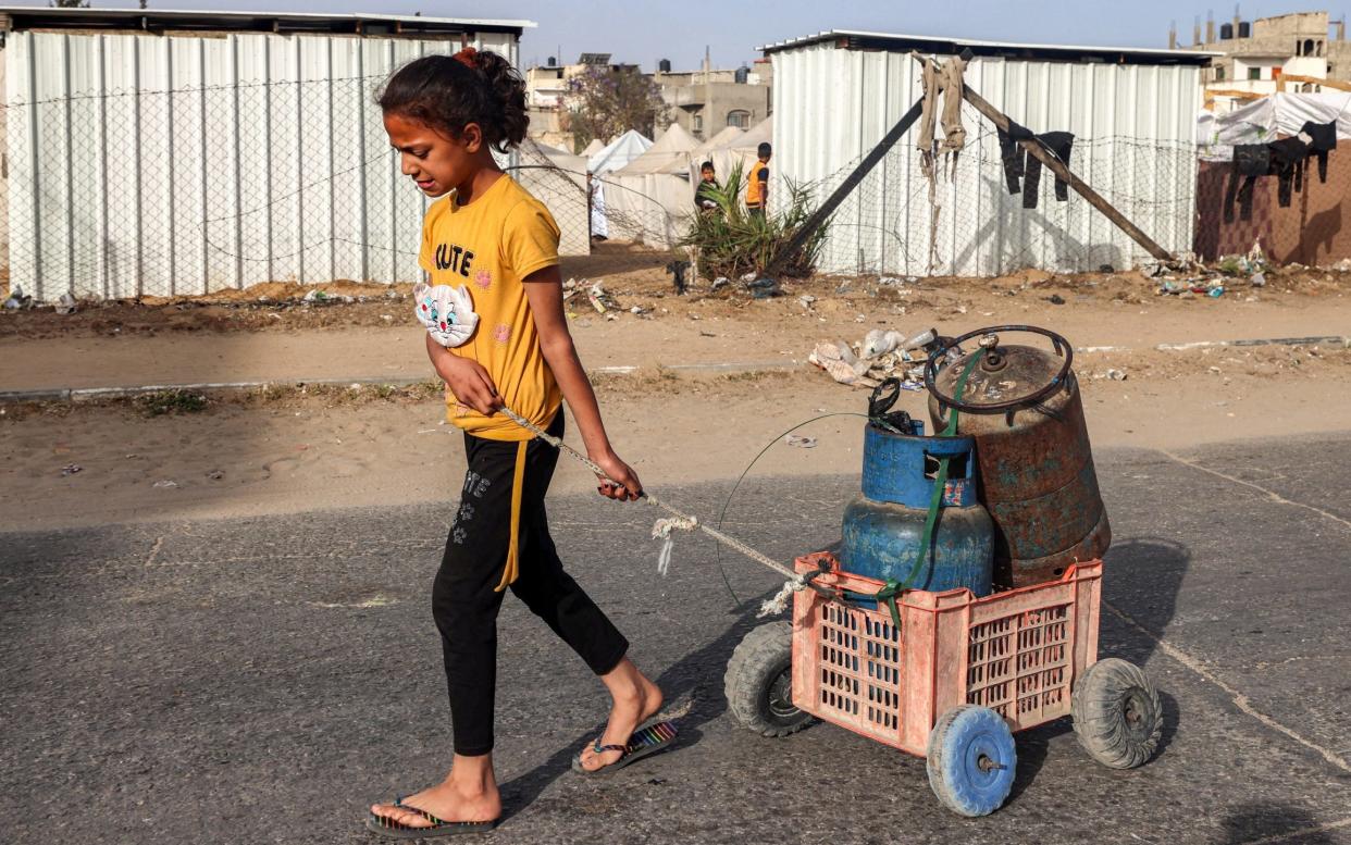 A girl pulls a cart loaded with gas cylinders along a street in Rafah