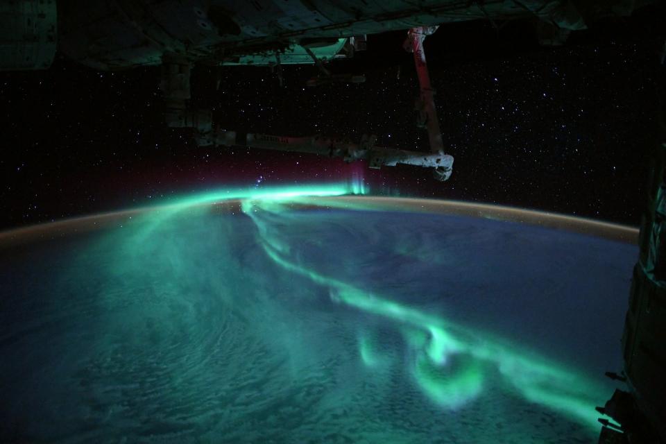 The international space station flying above bluish green auroras over Earth's southern hemisphere.