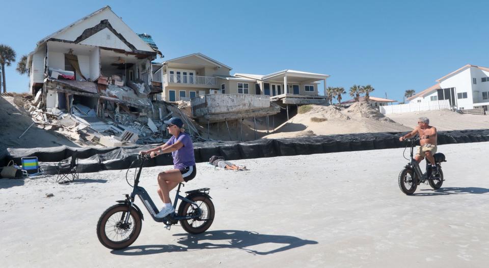 Beachgoers on e-bikes ride past damaged homes in the 4100 block of South Atlantic Avenue in hard-hit Wilbur-by-the-Sea. A year after Tropical Storm Nicole, repair work continues for some homeowners and business owners in Volusia and Flagler counties.