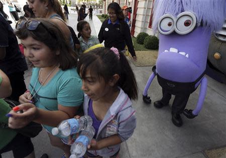 Girls walk past a purple Minion character at the new "Despicable Me Minion Mayhem" ride during technical rehearsals for the new attraction at Universal Studios Hollywood in Universal City, California March 28, 2014. REUTERS/Jonathan Alcorn