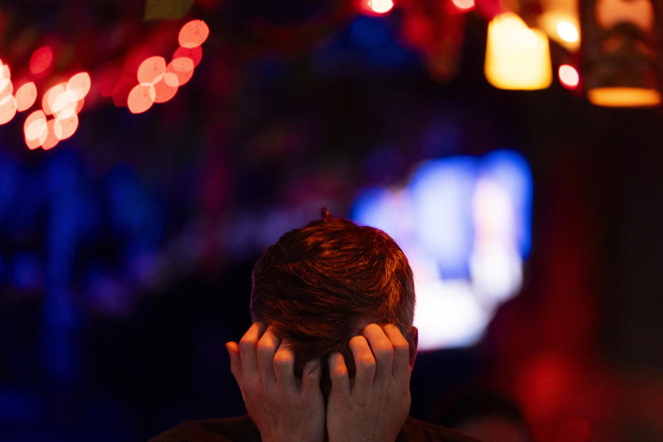 A person with short hair holds their head in their hands, surrounded by blurred lights in the background