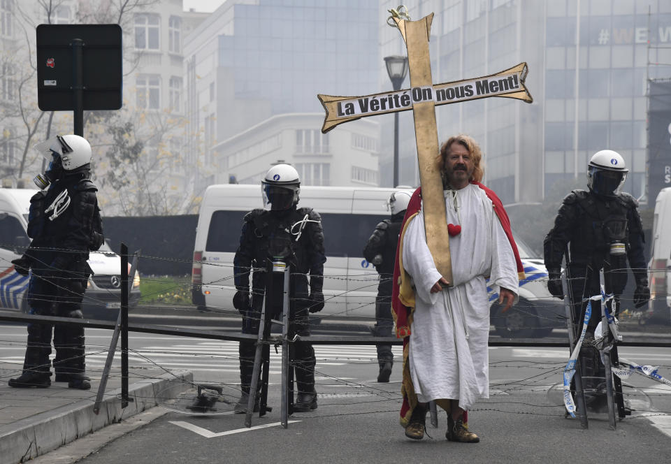 A protestor marches with a cross near EU headquarters during a demonstration against COVID-19 measures in Brussels, Sunday, Jan. 23, 2022. Demonstrators gathered in the Belgian capital to protest what they regard as overly extreme measures by the government to fight the COVID-19 pandemic, including a vaccine pass regulating access to certain places and activities and possible compulsory vaccines. Cross reads 'The truth we are being lied to about'. (AP Photo/Geert Vanden Wijngaert)