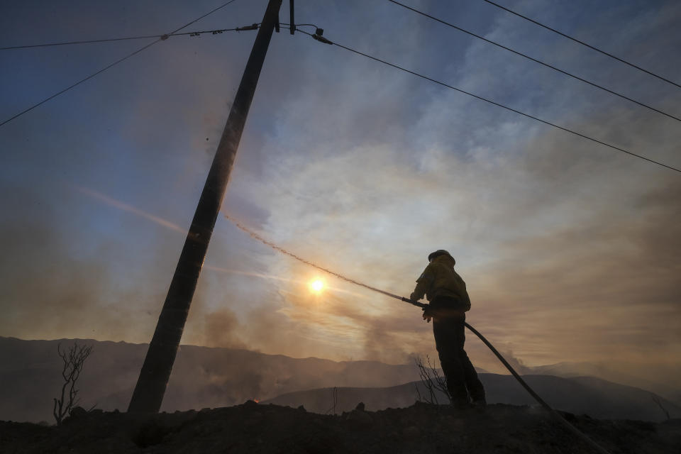 A firefighter sprays water on a power pole during a wildfire in Castaic, Calif. on Wednesday, Aug. 31, 2022. (AP Photo/Ringo H.W. Chiu)