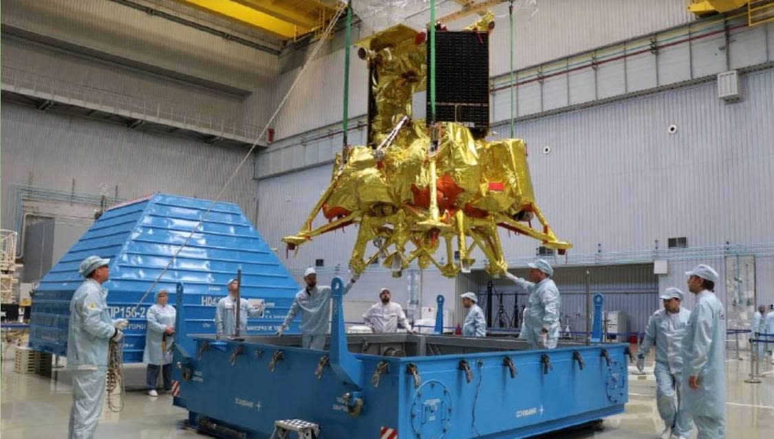  lab technicians in clean suits work on a gold-foil-wrapped spacecraft 