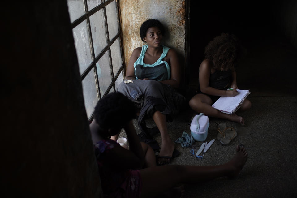 A mother sits on a window seat as she accompanies her daughter inside an occupied building where they live, in Rio de Janeiro, Brazil, Thursday, March 11, 2021. Brazilian women face worse labor choices or require flexible hours to raise their children, particularly since public schools provide only half days of classes. (AP Photo/Silvia Izquierdo)