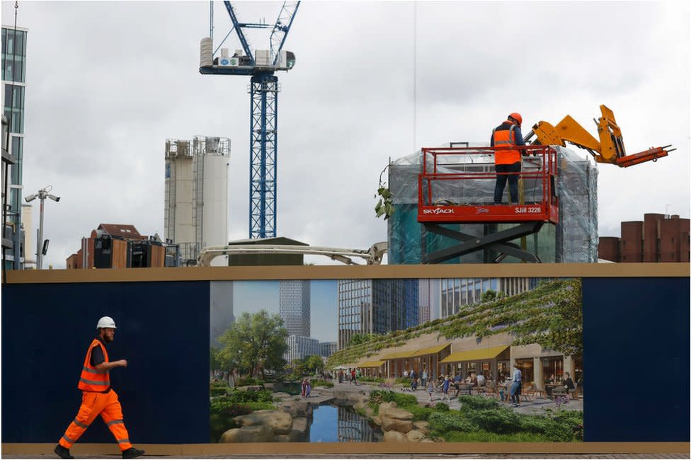 A construction worker passes a hoarding surrounding the One Thames City development in London