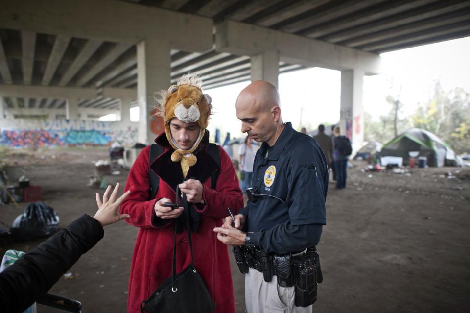 In this Monday, Dec. 9, 2013 photo, Savannah Metro Police Department Homeless Liaison Officer Tom Gentner, right, gathers contact information from a young couple who are living in homeless Camp 8 South under the ramps of the Truman Parkway in Savannah, Ga. Since September 2013 the Savannah police department gave Gentner the task of keeping track of over three hundred homeless people living near the historic downtown area. The couple later found temporary housing with the help of Gentner. (AP Photo/Stephen B. Morton)