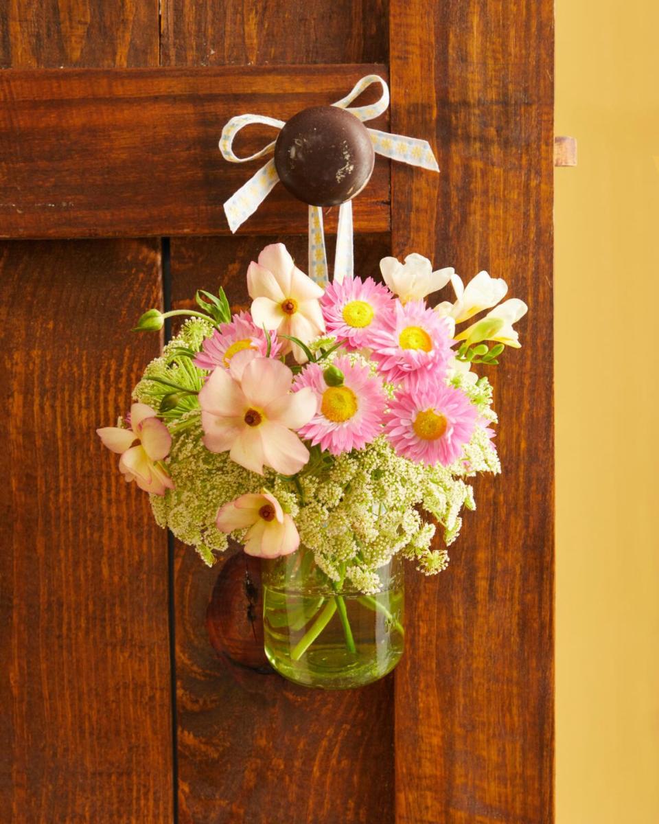 a bouquet of flowers arranged in a vintage green mason jar hung from a ribbon on a brown door
