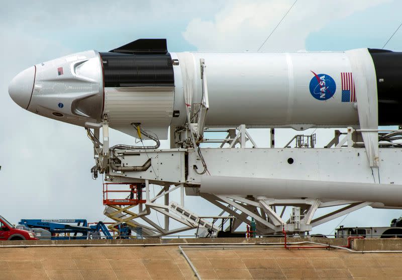 Crews work on the SpaceX Crew Dragon, attached to a Falcon 9 booster rocket, as it sits horizontal on Pad39A