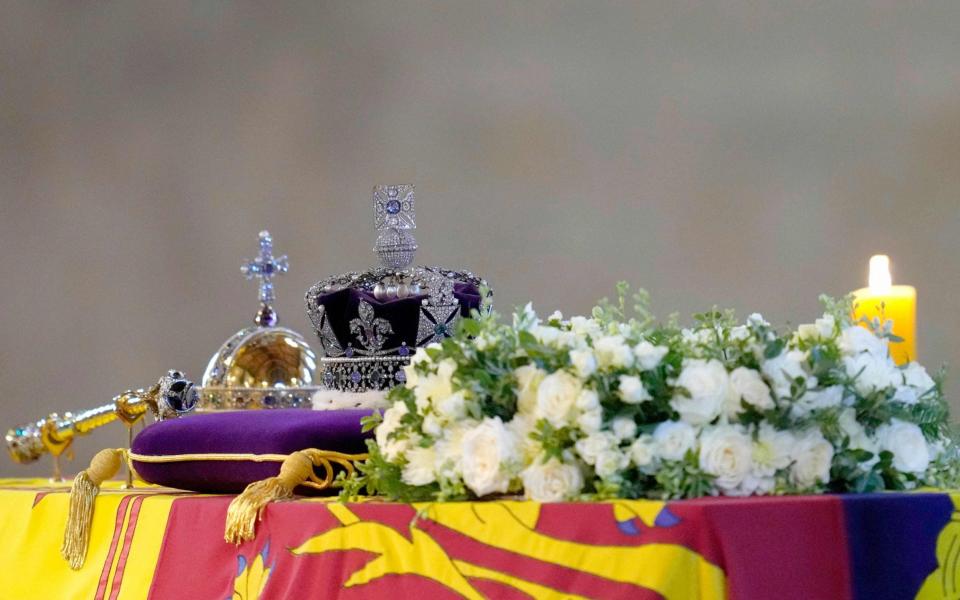 The coffin of Queen Elizabeth II, draped in the Royal Standard with the Imperial State Crown and the Sovereign's orb and sceptre, lies in state on the catafalque as members of the public move past in Westminster Hall, at the Palace of Westminster - AFP
