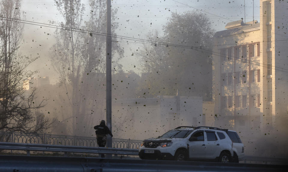 A police officer watches stone and earth debris flying through the air as Russian kamikaze drones hit the centre of the capital Kyiv, Ukraine, Monday, Oct. 17, 2022. (AP Photo/Vadym Sarakhan)