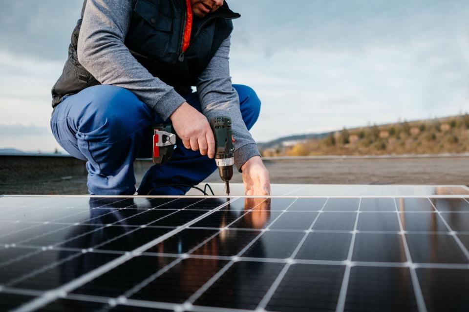 A worker installs solar panels using a drill. 