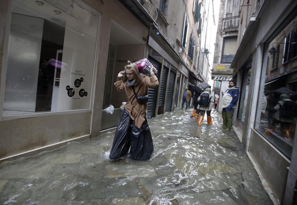 A woman wears bin bags as she carries her suitcase while wading through high water, in Venice, Wednesday, Nov. 13, 2019. The high-water mark hit 187 centimeters (74 inches) late Tuesday, Nov. 12, 2019, meaning more than 85% of the city was flooded. The highest level ever recorded was 194 centimeters (76 inches) during infamous flooding in 1966. (AP Photo/Luca Bruno)