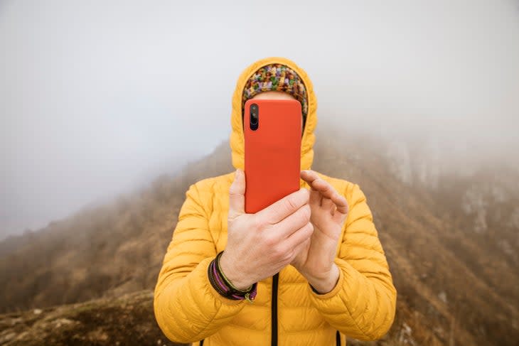 man with yellow hooded down jacket photographing with smartphone 