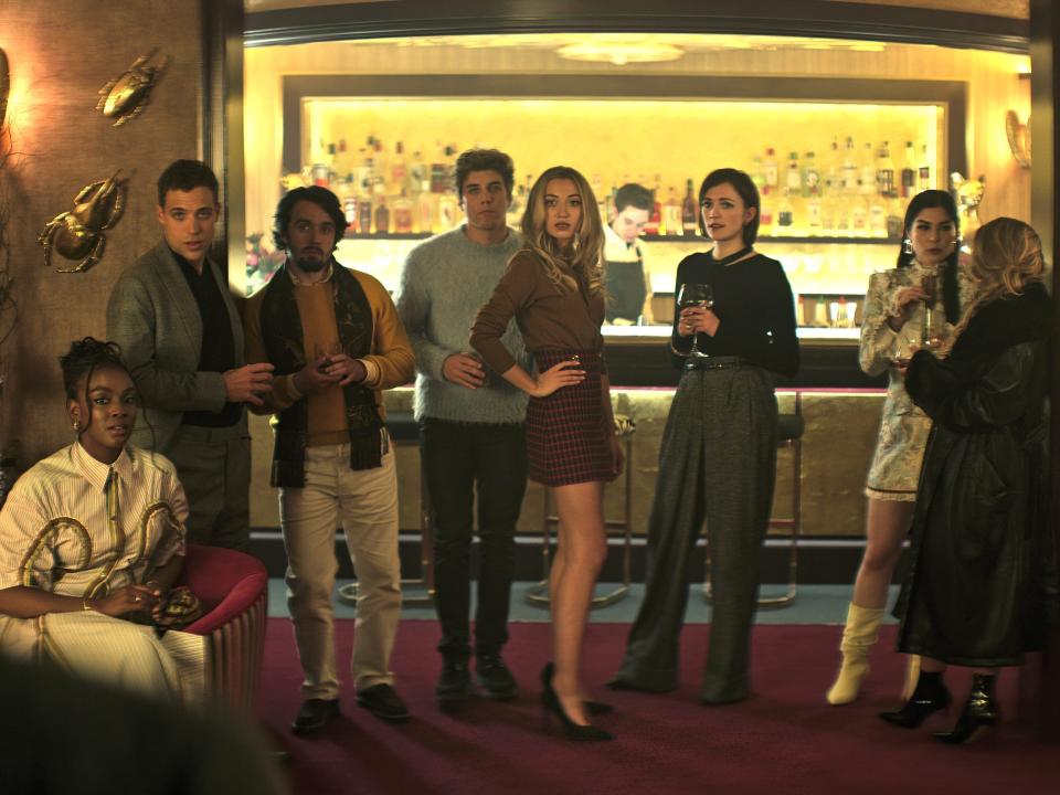 A diverse group of young British aristocrats stands at a bar in a scene from the show "You."