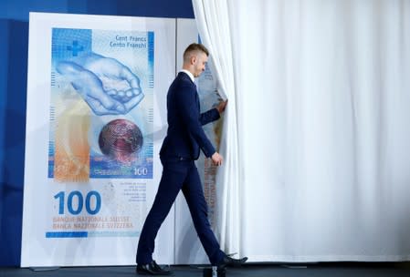 An employee of the Swiss National Bank unveils the new 100 franc banknote during a news conference in Bern