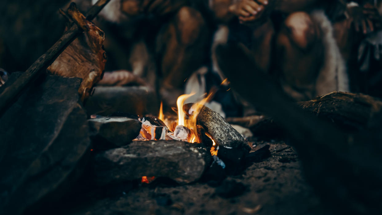 Close-up of Tribe Prehistoric Hunter-Gatherers Trying to Get Warm at the Bonfire, Holding Hands over Fire, Cooking Food. Neanderthal or Homo Sapiens Family Live in Cave at Night.