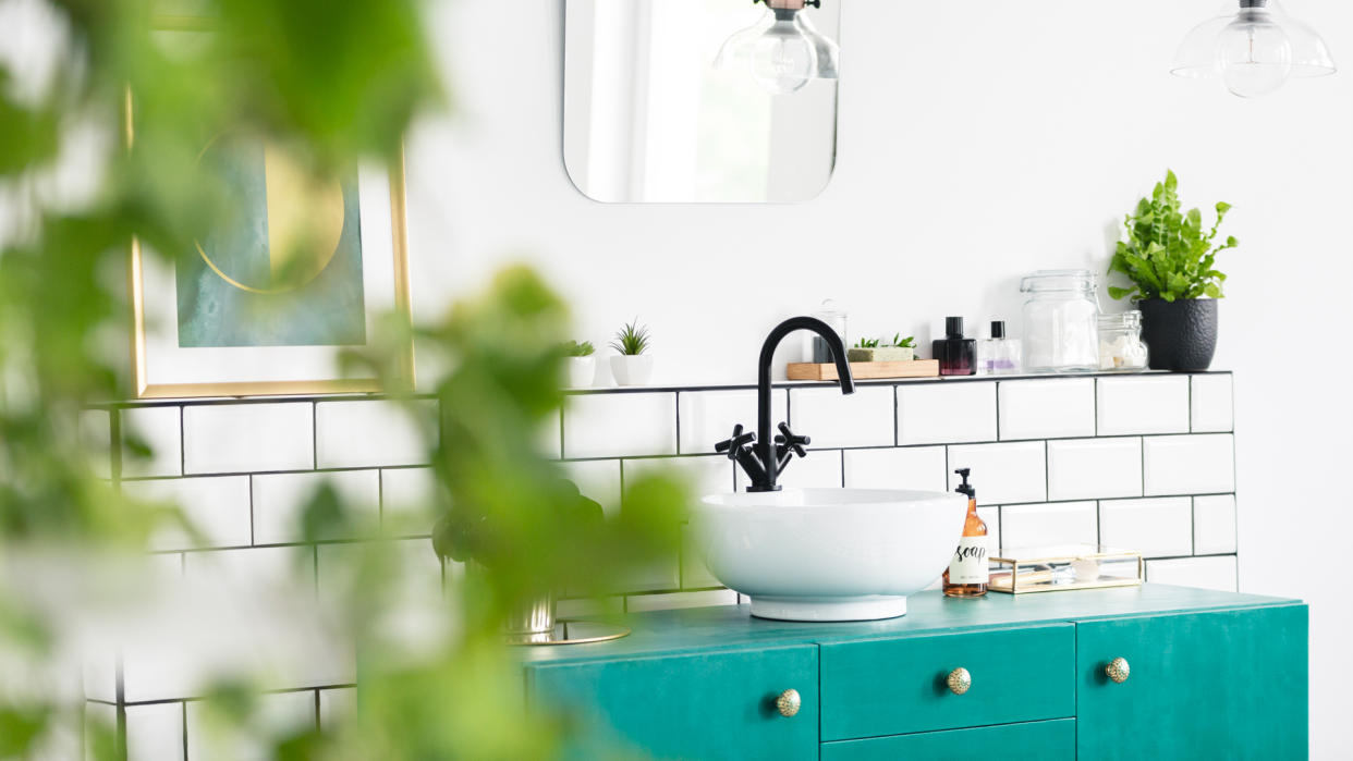 Close-up of blurred leaves with a sink, green cupboard and mirror in the background in the bathroom interior.