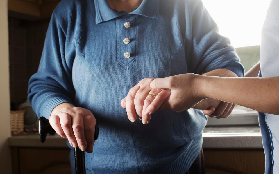 A personal care assistant helps an elderly woman to walk - Getty