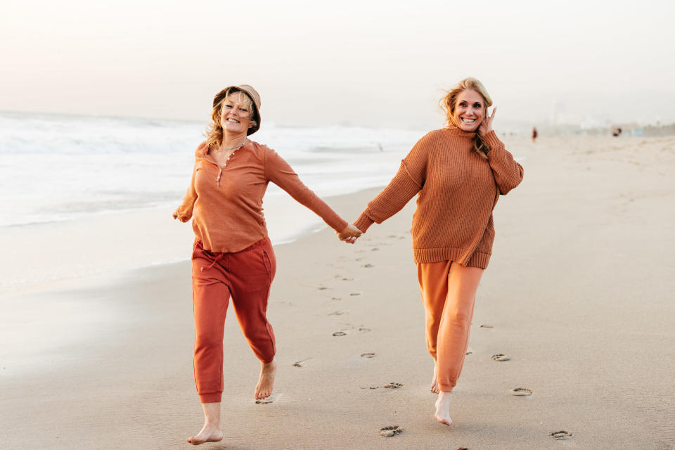 Two women hold hands as they run along the beach