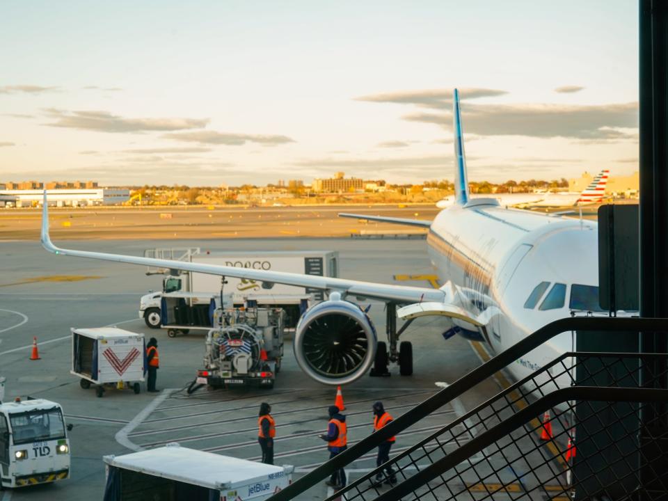 A JetBlue plane parked at a gate with a sunset in the background