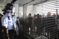 Police watch demonstrators through a closed entrance gate at the Kwun Tong MTR station in Hong Kong, Saturday, Aug. 24, 2019. Chinese police said Saturday they released an employee at the British Consulate in Hong Kong as the city's pro-democracy protesters took to the streets again, this time to call for the removal of "smart lampposts" that raised fears of stepped-up surveillance. (AP Photo/Kin Cheung)