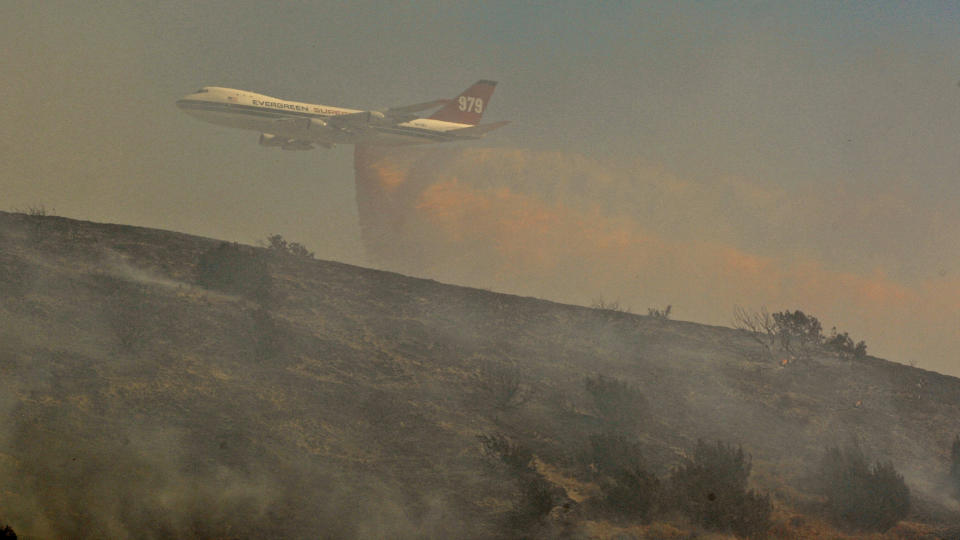 FILE - In this July 30, 2010, file photo, a Boeing Evergreen B-747 Supertanker drops fire retardant over a hillside subdivision on the outskirts of Palmdale, Calif. A report released Friday, Sept. 14, 2018, by California’s firefighting agency says firefighter Mathew Burchett was killed on Aug. 13, by a tree uprooted when thousands of gallons of flame-suppressing liquid were dropped from a similar Boeing 747 flying only 100 feet above the treetops at the Mendocino Complex fire north of San Francisco. (AP Photo/Damian Dovarganes, File)