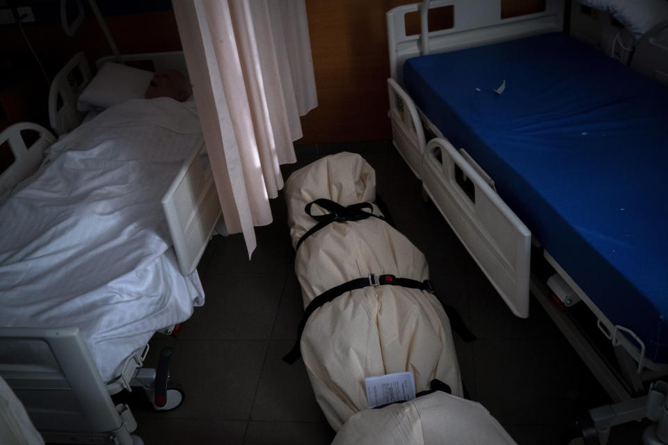 A person sleeps in a bed a few feet away from a body sealed in bags on the floor of a nursing home in Barcelona, Spain, Thursday, Nov. 19, 2020. (AP Photo/Emilio Morenatti)