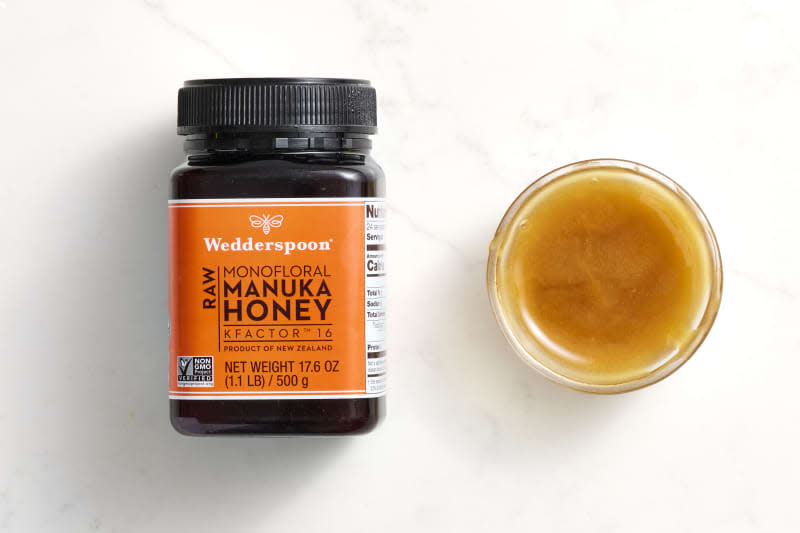 overhead shot of Wedderspoon Raw monofloral manuka honey in a bottle, and also some honey in a small glass bowl to the right of the bottle to show consistency.