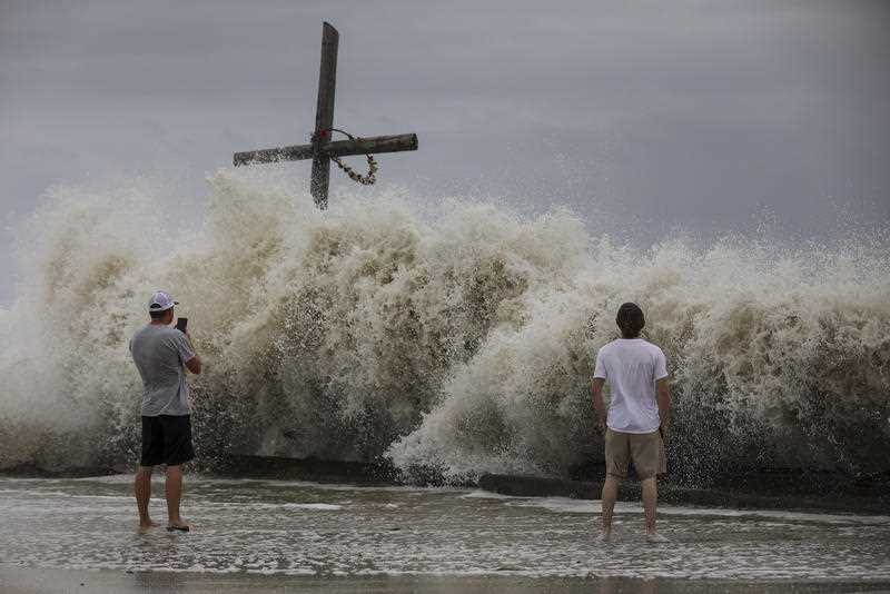 Mark Allums, left, and Hunter Clark watch waves crash ashore as outer bands from Hurricane Laura begin to hit the coast in High Island.