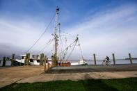 A man bicycles past the shrimp boat "Capt. T.J." owned by the 13 Mile Seafood company while it is docked in Apalachicola, Florida