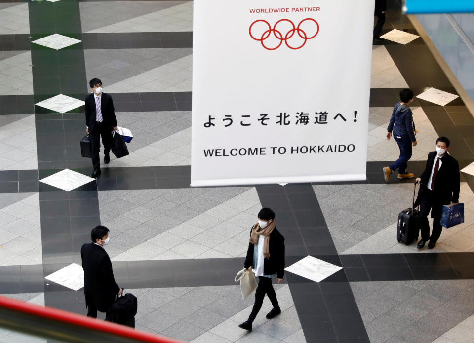 Passengers wearing protective face masks, following an outbreak of the coronavirus, walk under a campaign banner for Tokyo 2020 Olympic Games at New Chitose Airport in Chitose, Hokkaido, northern Japan February 27, 2020. REUTERS/Issei Kato